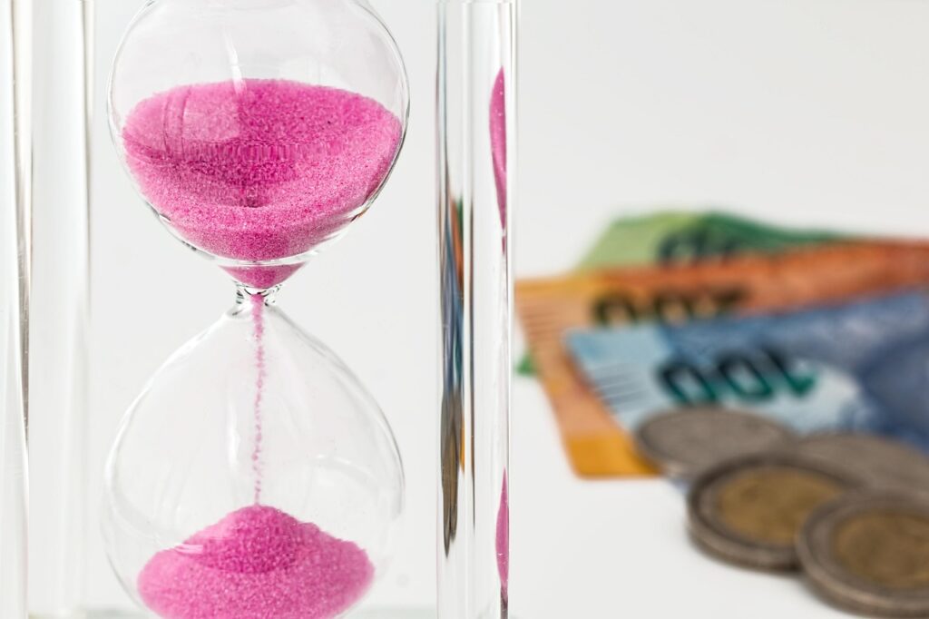 Sablier avec du sable rose s'écoulant juste à coté de billet d'argent et de monnaies.